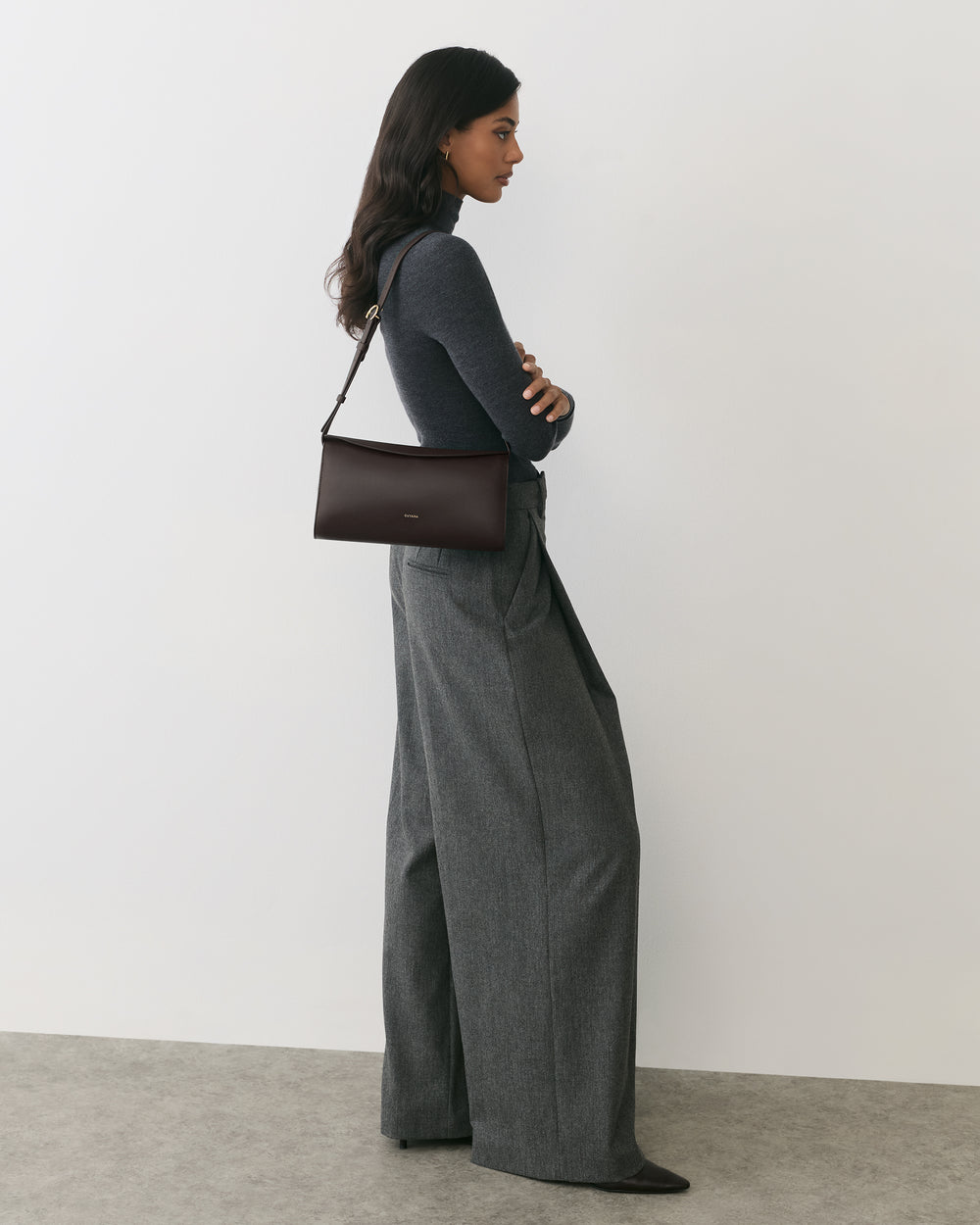 Person in wide-legged pants wearing a shoulder bag, standing against a plain background.