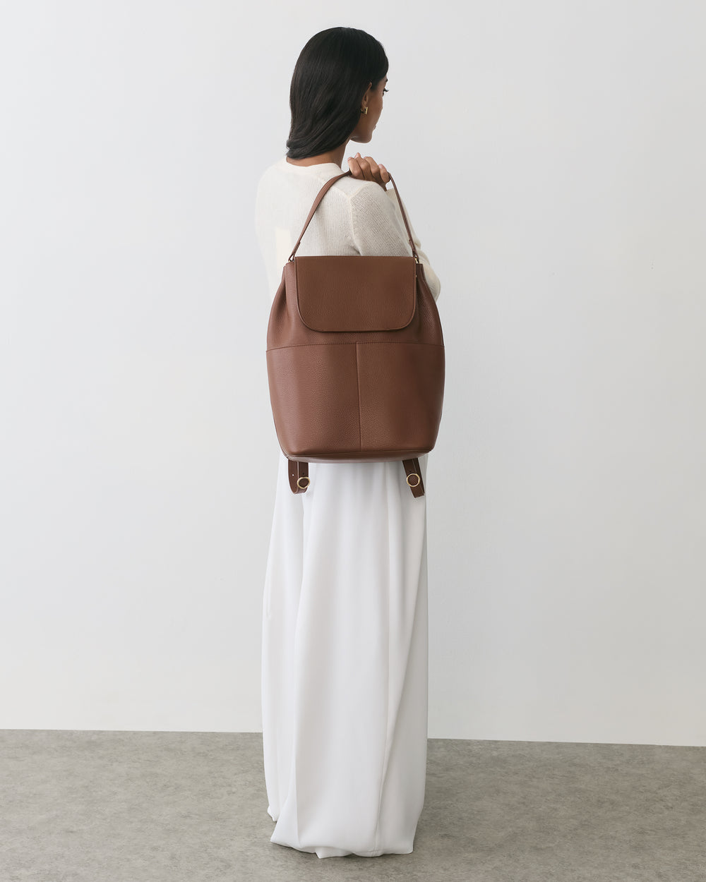 Person in a long dress holding a large bag with both hands, looking away.