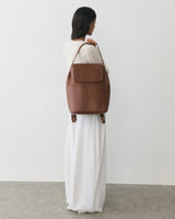 Person in a long dress holding a large bag with both hands, looking away.