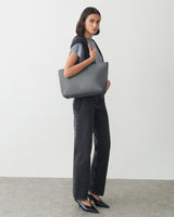 Person standing with shoulder bag and wearing a top and jeans.