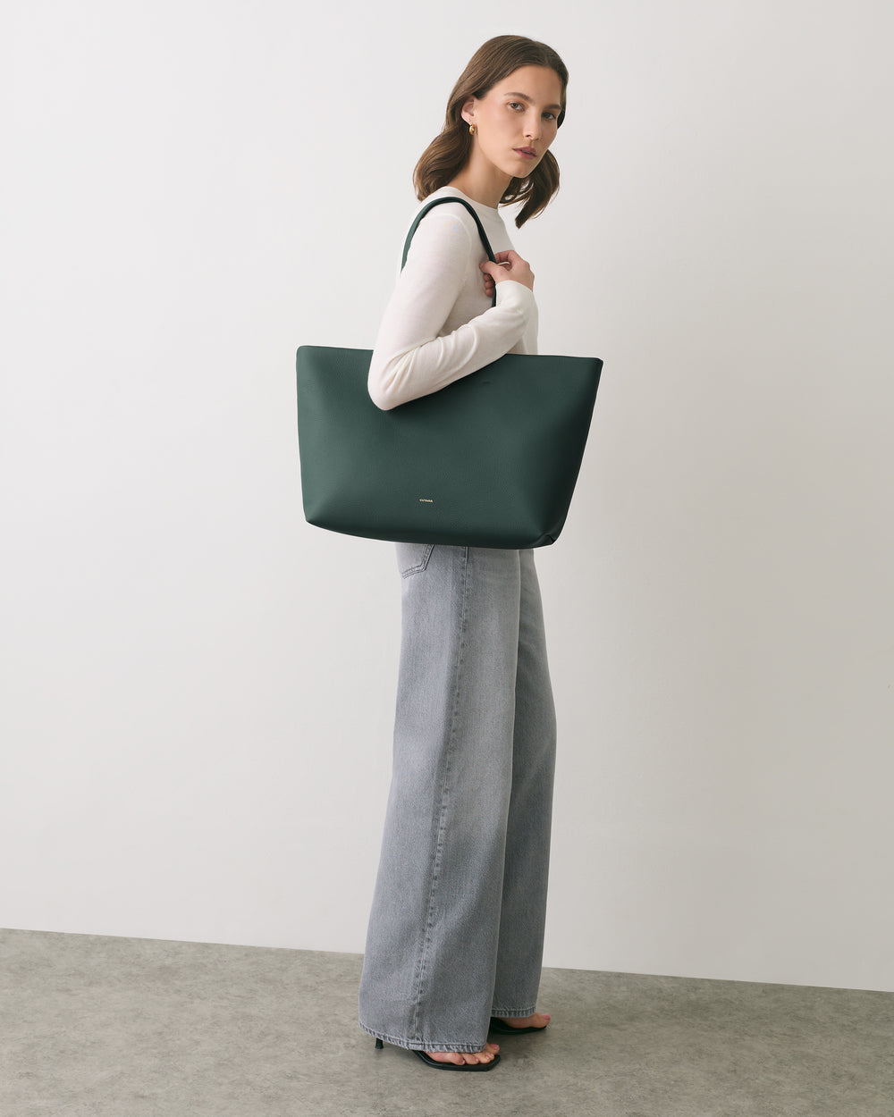 Person holding large tote bag, wearing long-sleeve top and wide-leg pants.