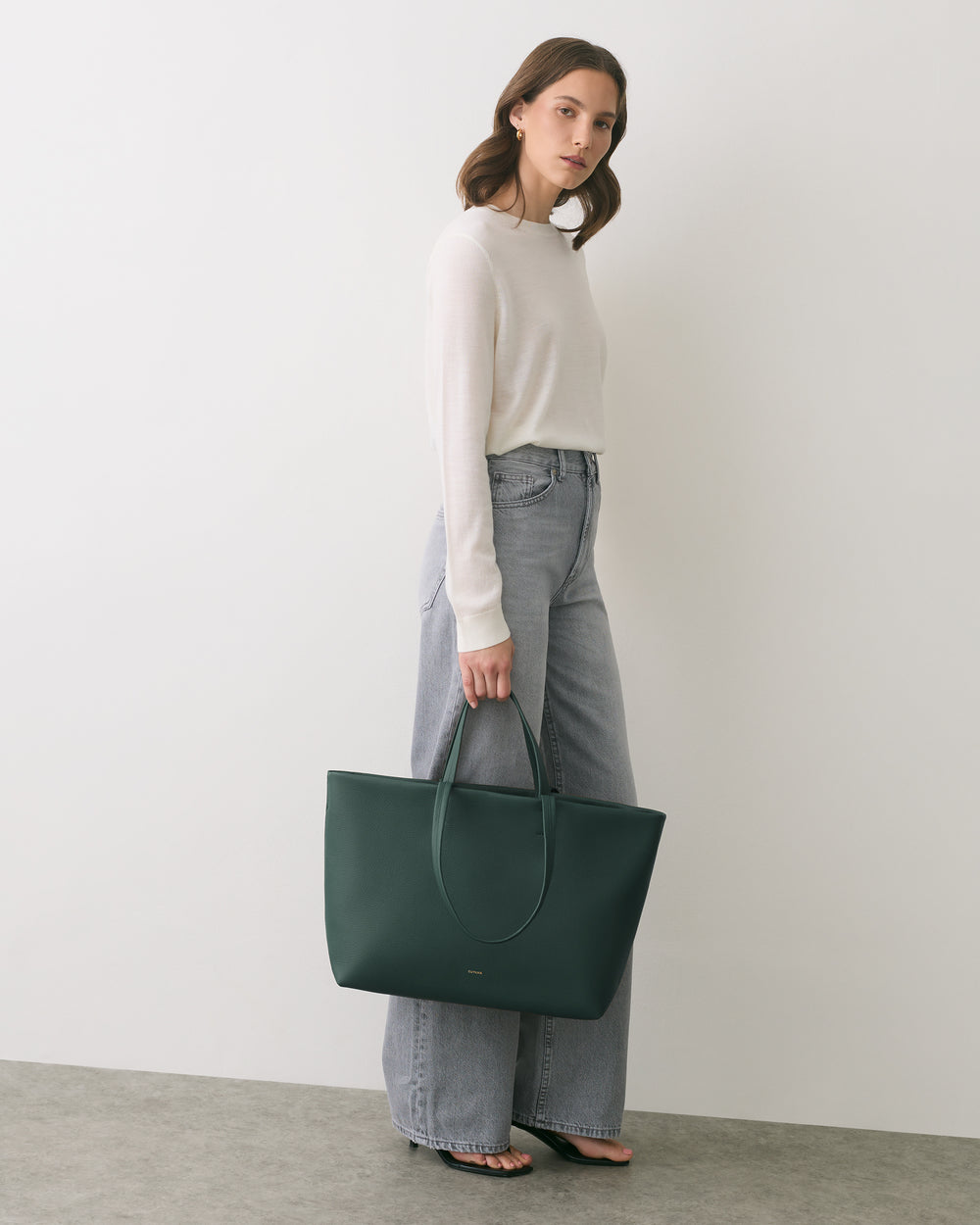 Person holding a large tote bag while standing against a plain wall.