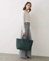 Person holding a large tote bag while standing against a plain wall.