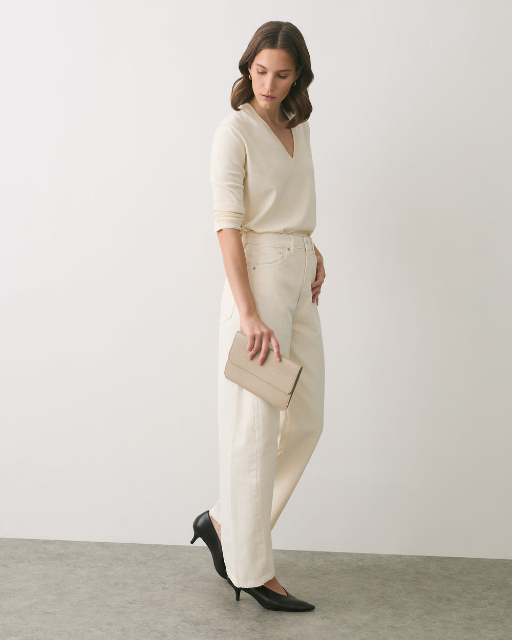 Person in a V-neck shirt and pants holding a clutch wearing heels standing indoors.