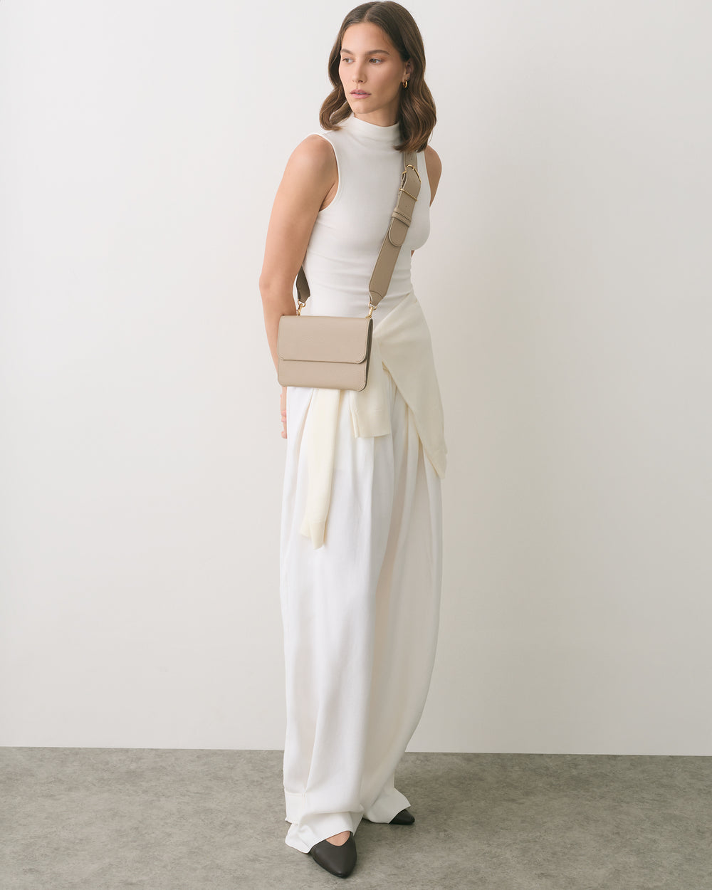 Person wearing a sleeveless top, long skirt, and crossbody bag standing indoors.