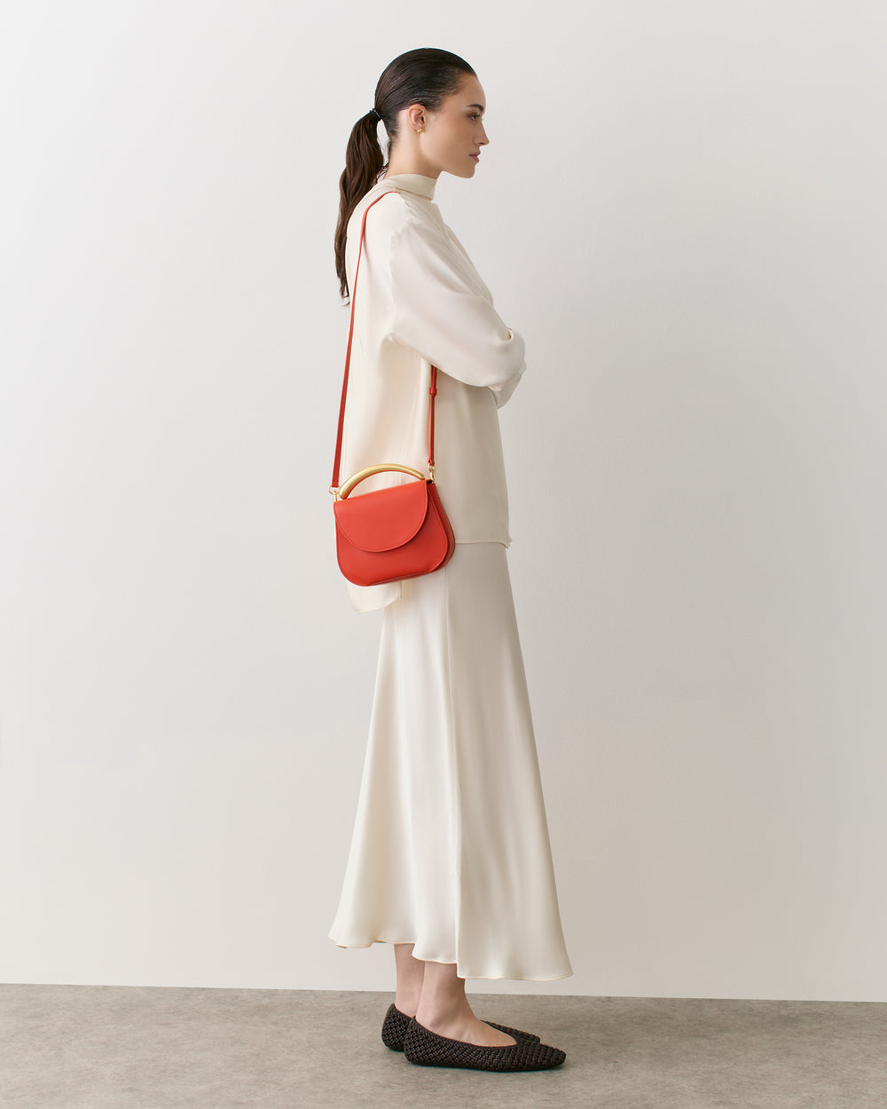 Person in a long sleeve outfit with a small shoulder bag facing left