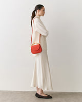 Person in a long sleeve outfit with a small shoulder bag facing left
