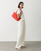 Person in light outfit holding a large handbag over shoulder.