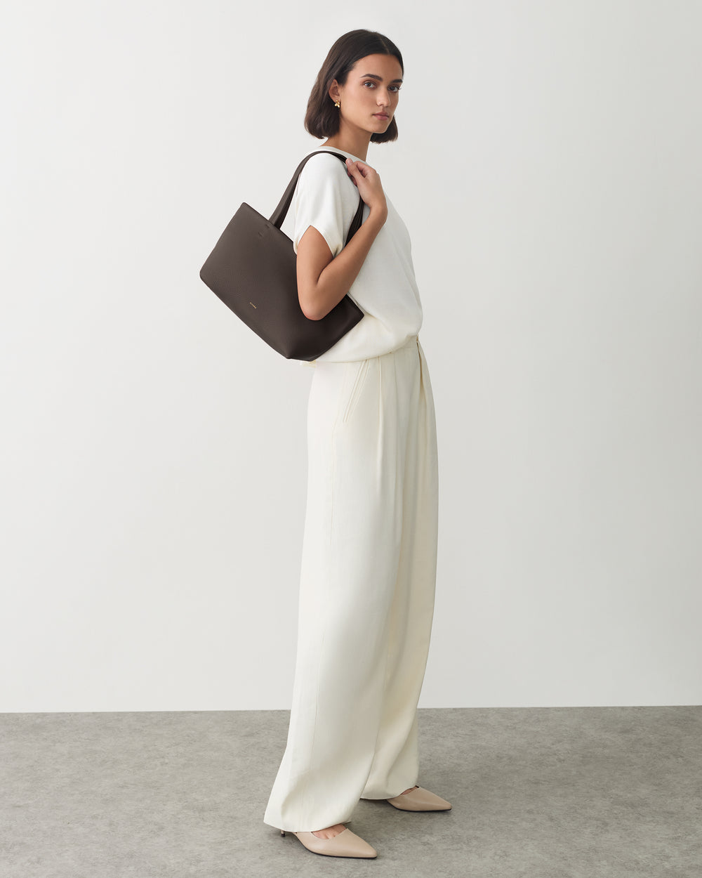 Person with shoulder bag wearing a top and wide-leg pants standing against a plain background.