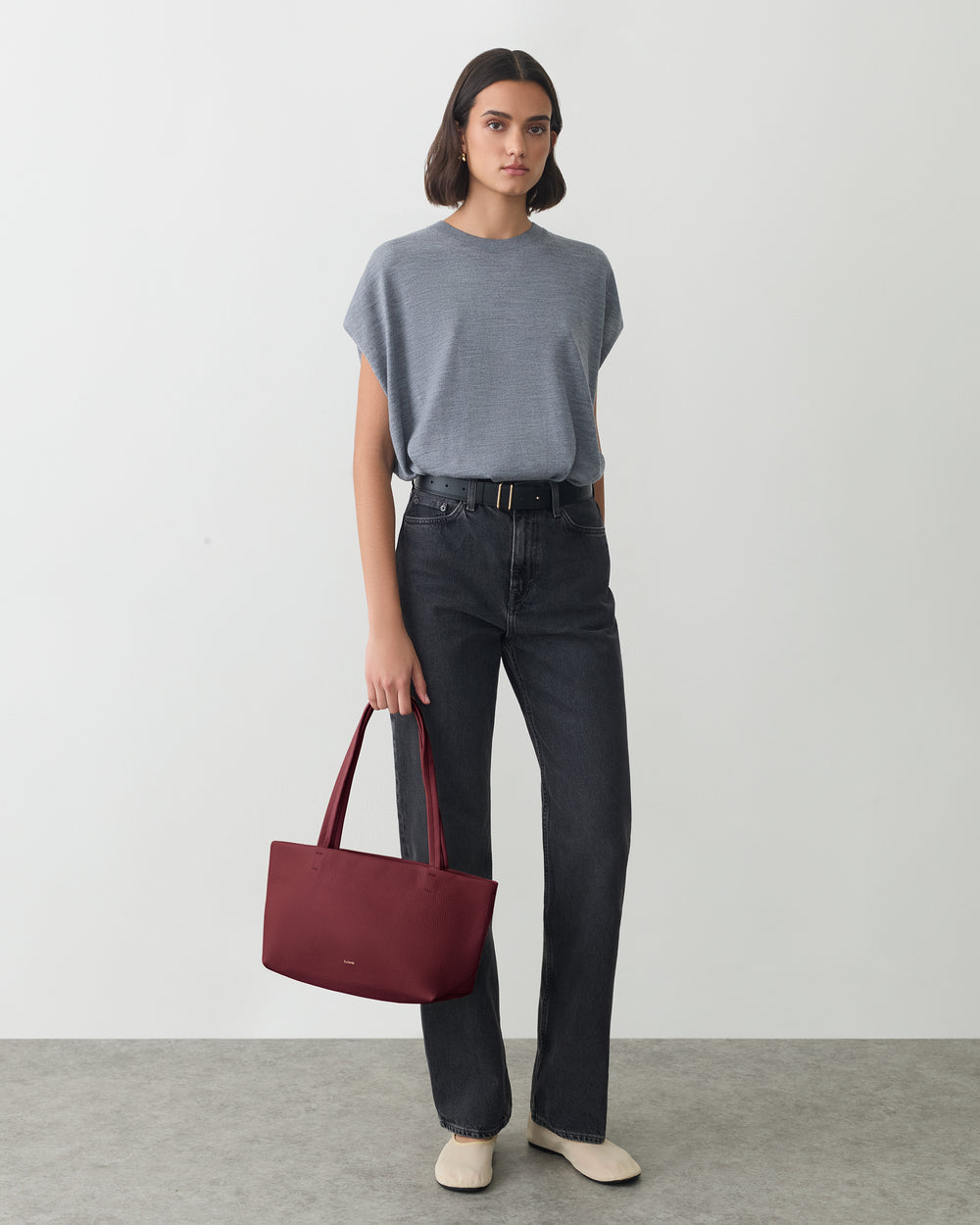 Person standing with a handbag, wearing a short-sleeve top and jeans.