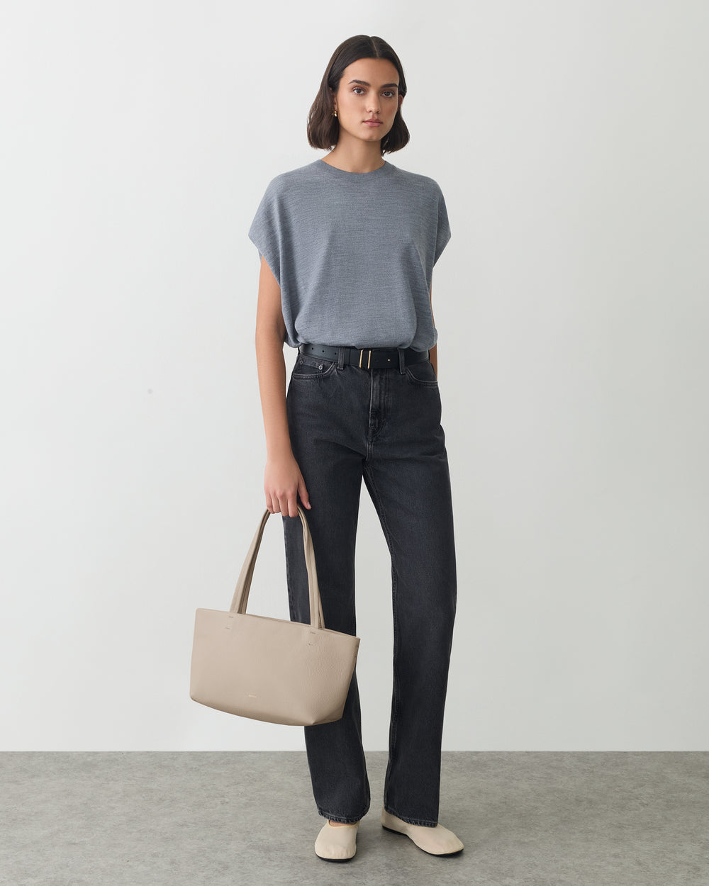 Person wearing a t-shirt and jeans holding a bag, standing indoors.