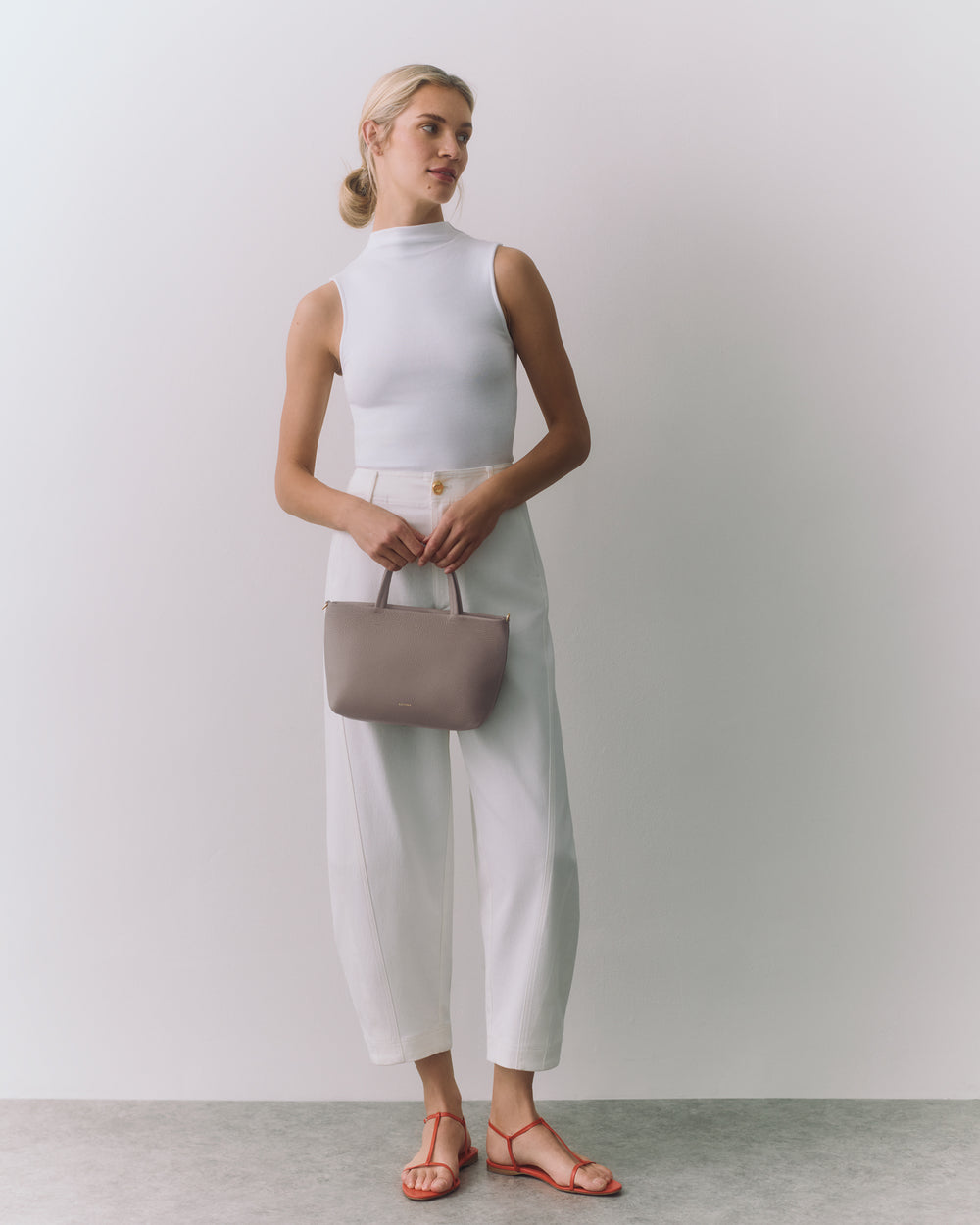Person in sleeveless top and pants holding a small bag.