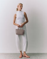 Person in sleeveless top and pants holding a small bag.