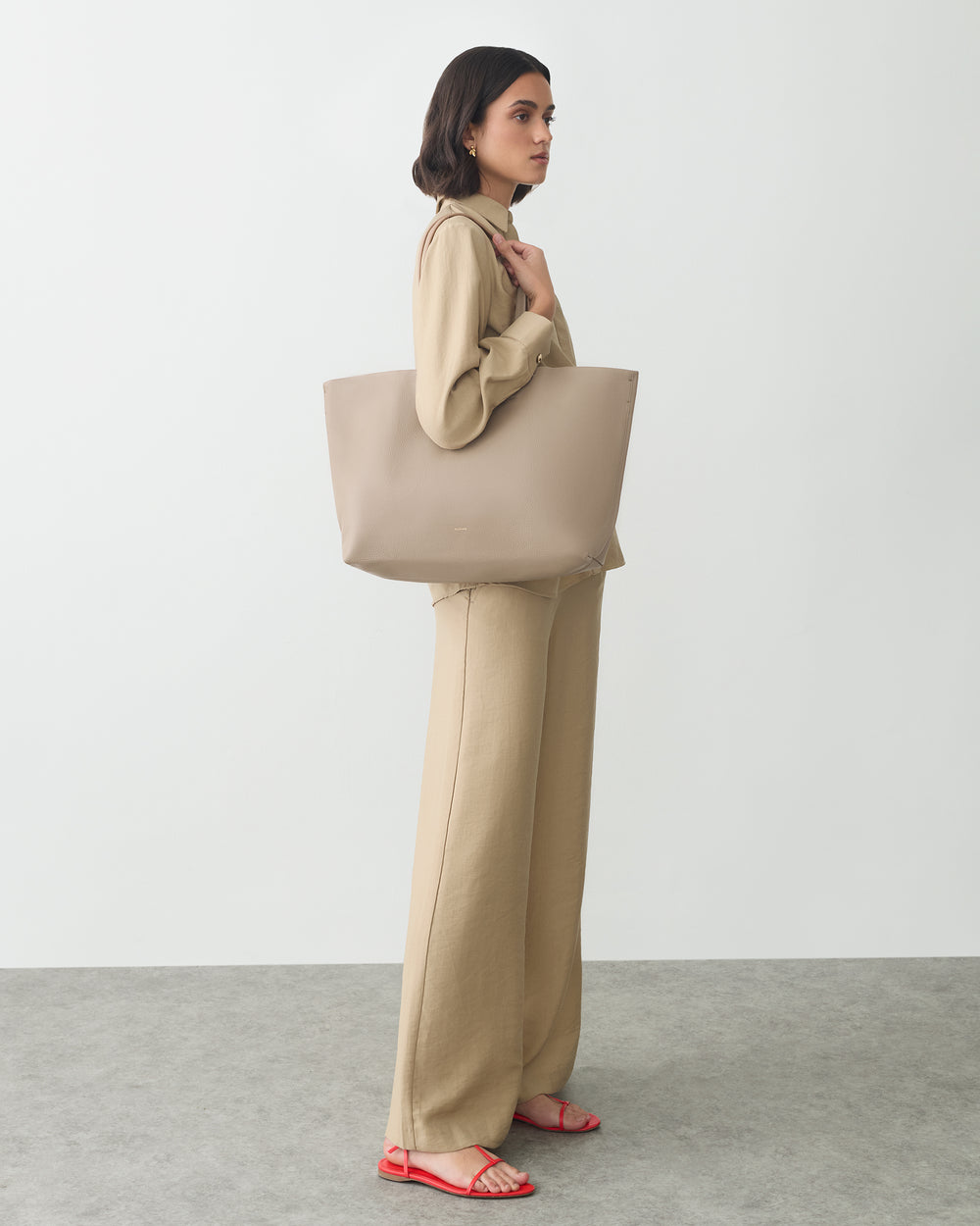 Person standing with tote bag wearing matching outfit and sandals.