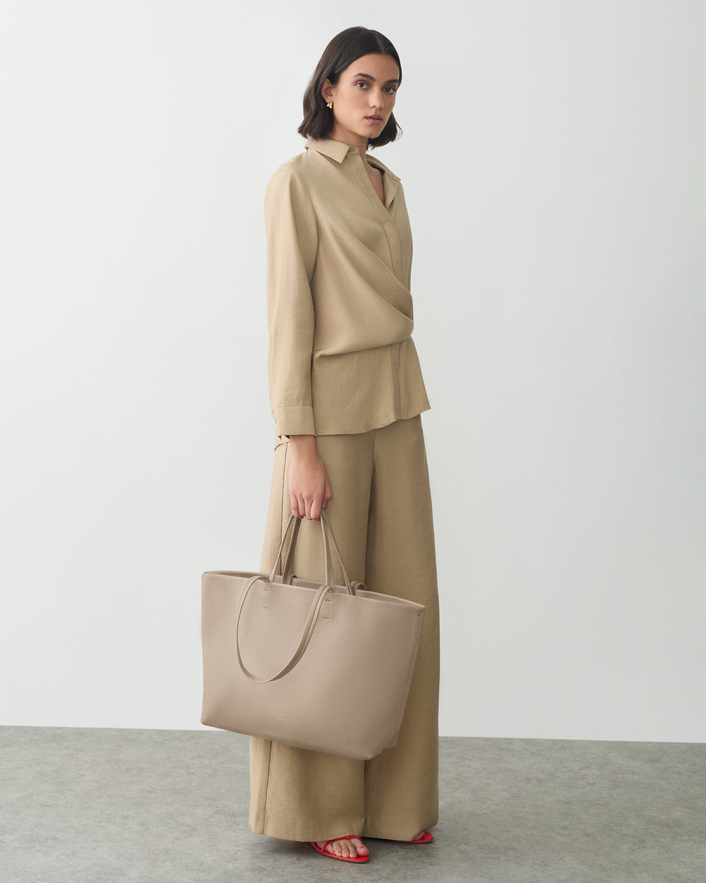 Woman in long-sleeve top and pants holding a tote bag.