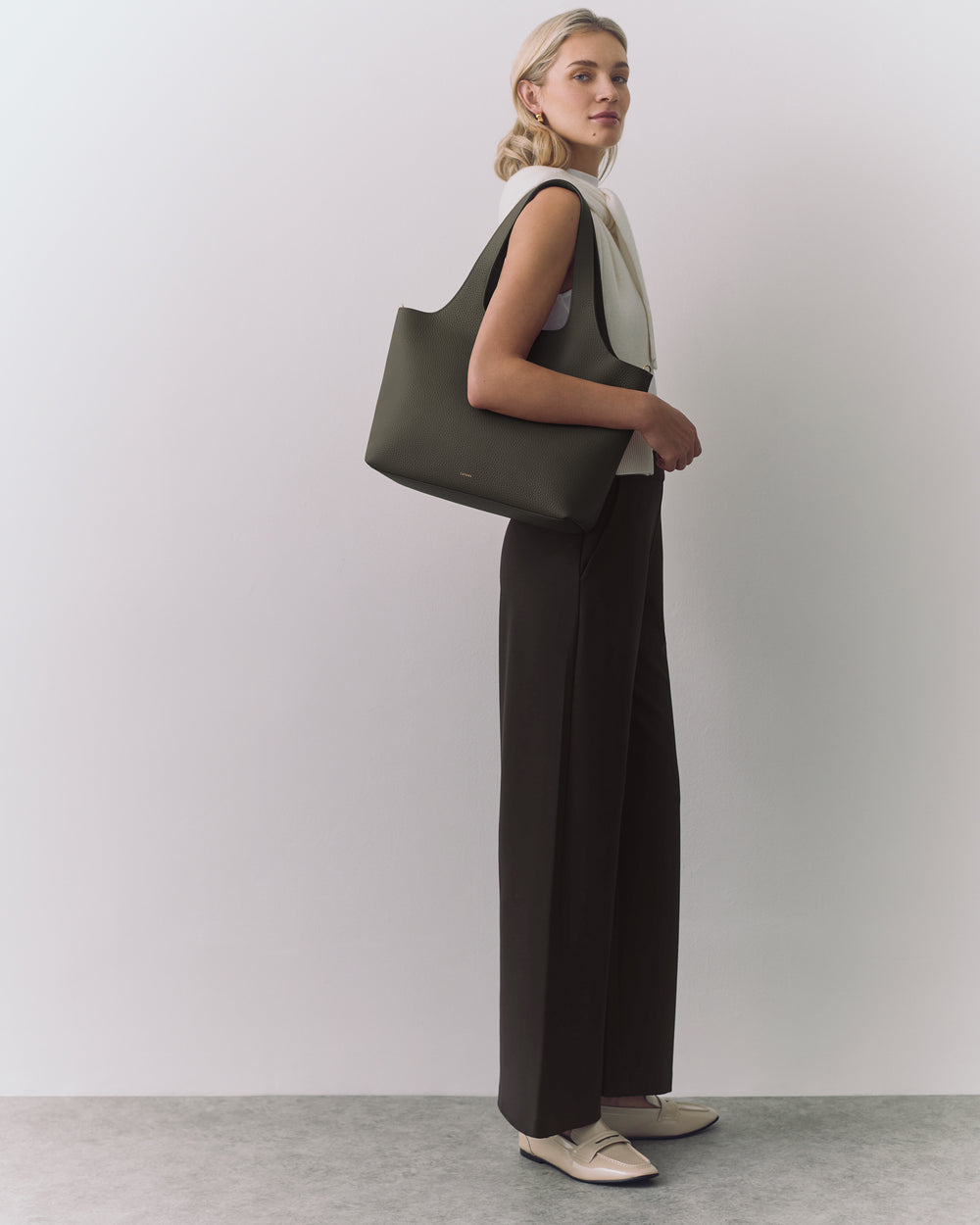 Person standing with a shoulder bag wearing sleeveless top and wide-leg pants.