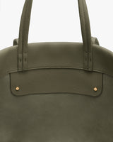 Close-up of a tote bag with short handles and gold studs on a flat surface.