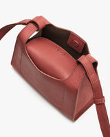 Open handbag with strap and button closure, showcasing main compartment inside.
