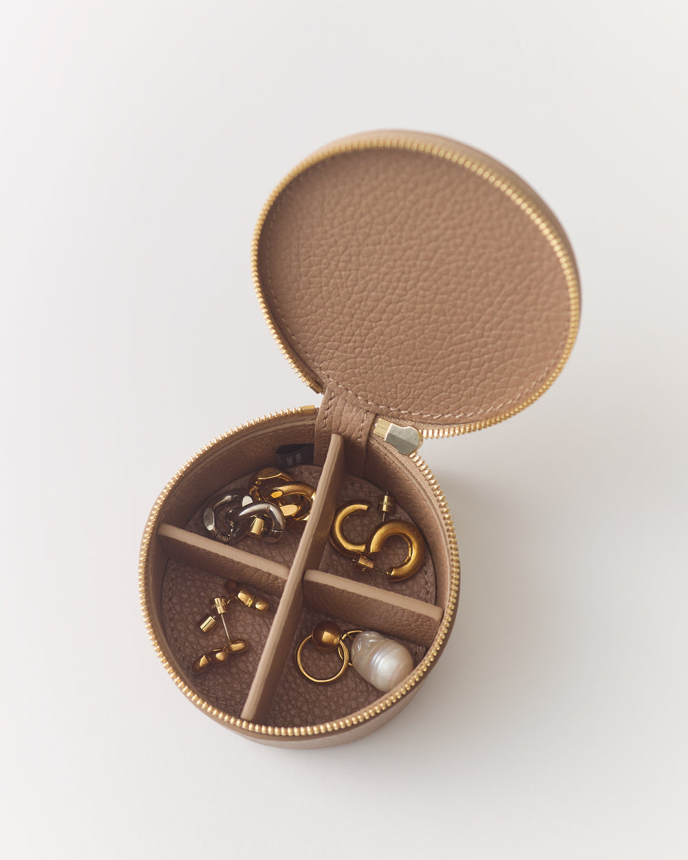 Round jewelry case with small compartments holding various earrings and rings.