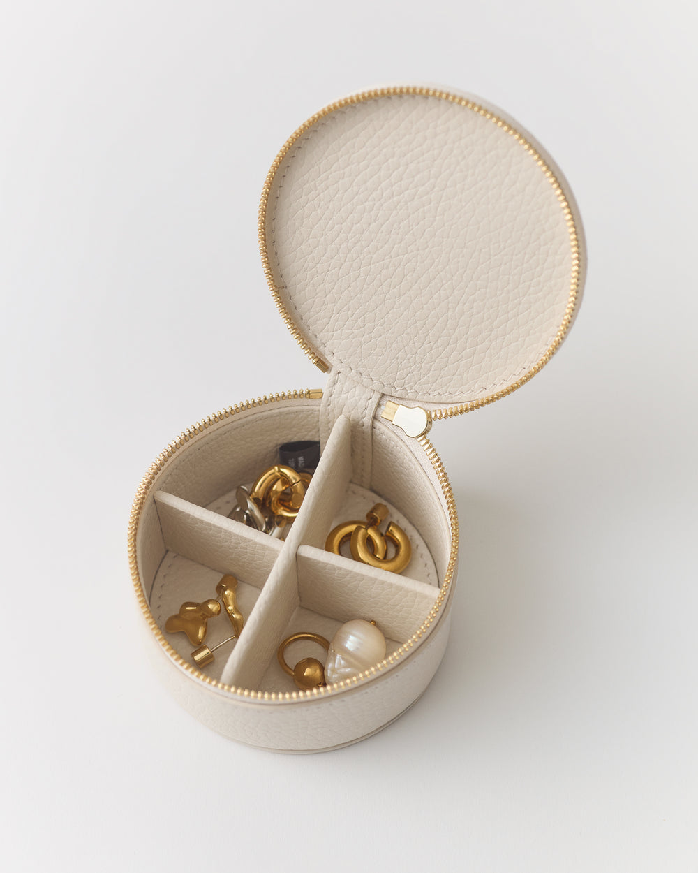 Round jewelry case with open lid showing compartments filled with various jewelry items.