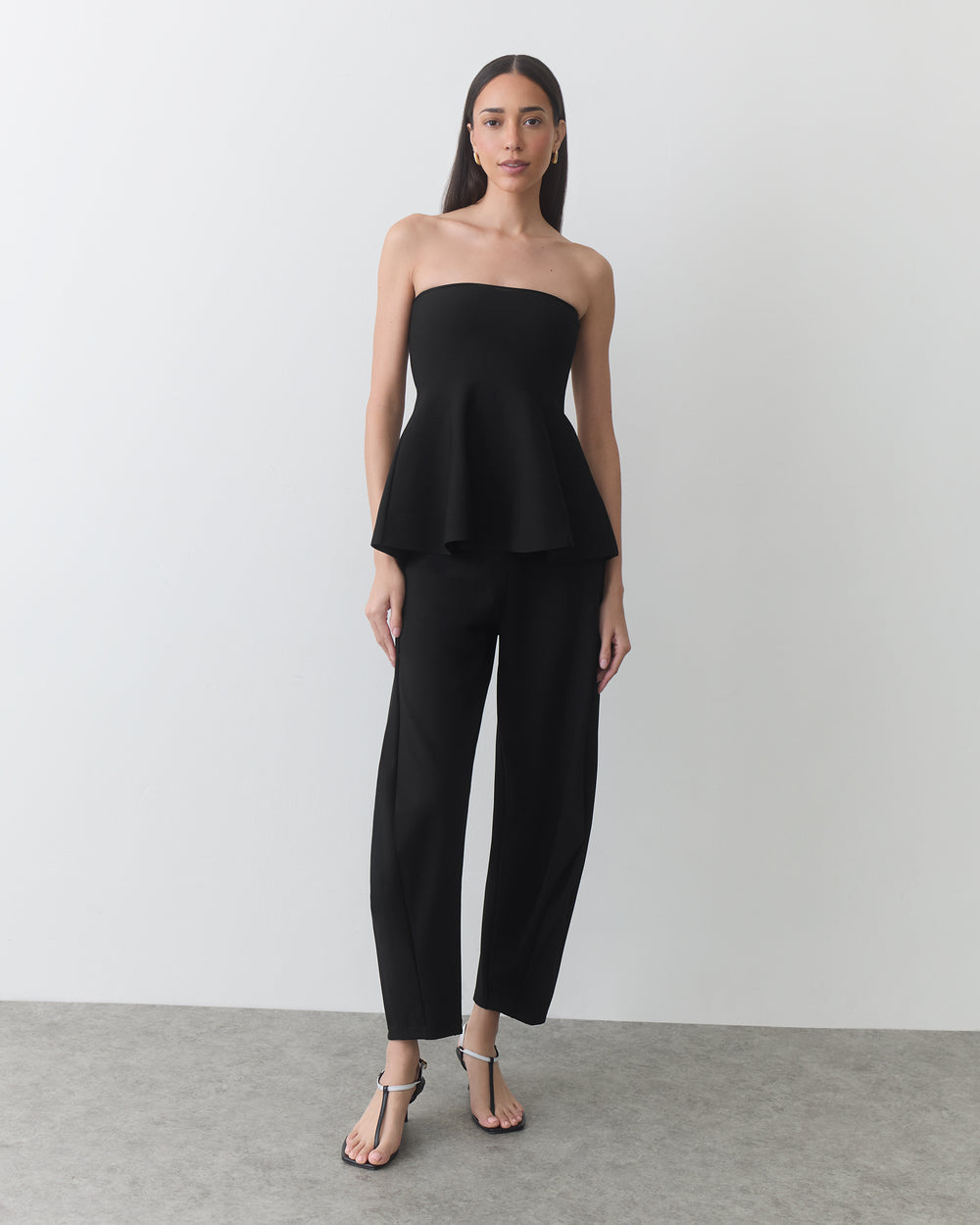 Person wearing a strapless top and pants with open-toe footwear stands in a room.