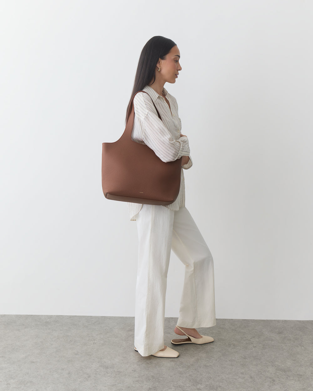 Person holding a large handbag, wearing a long-sleeve top and wide-leg pants.