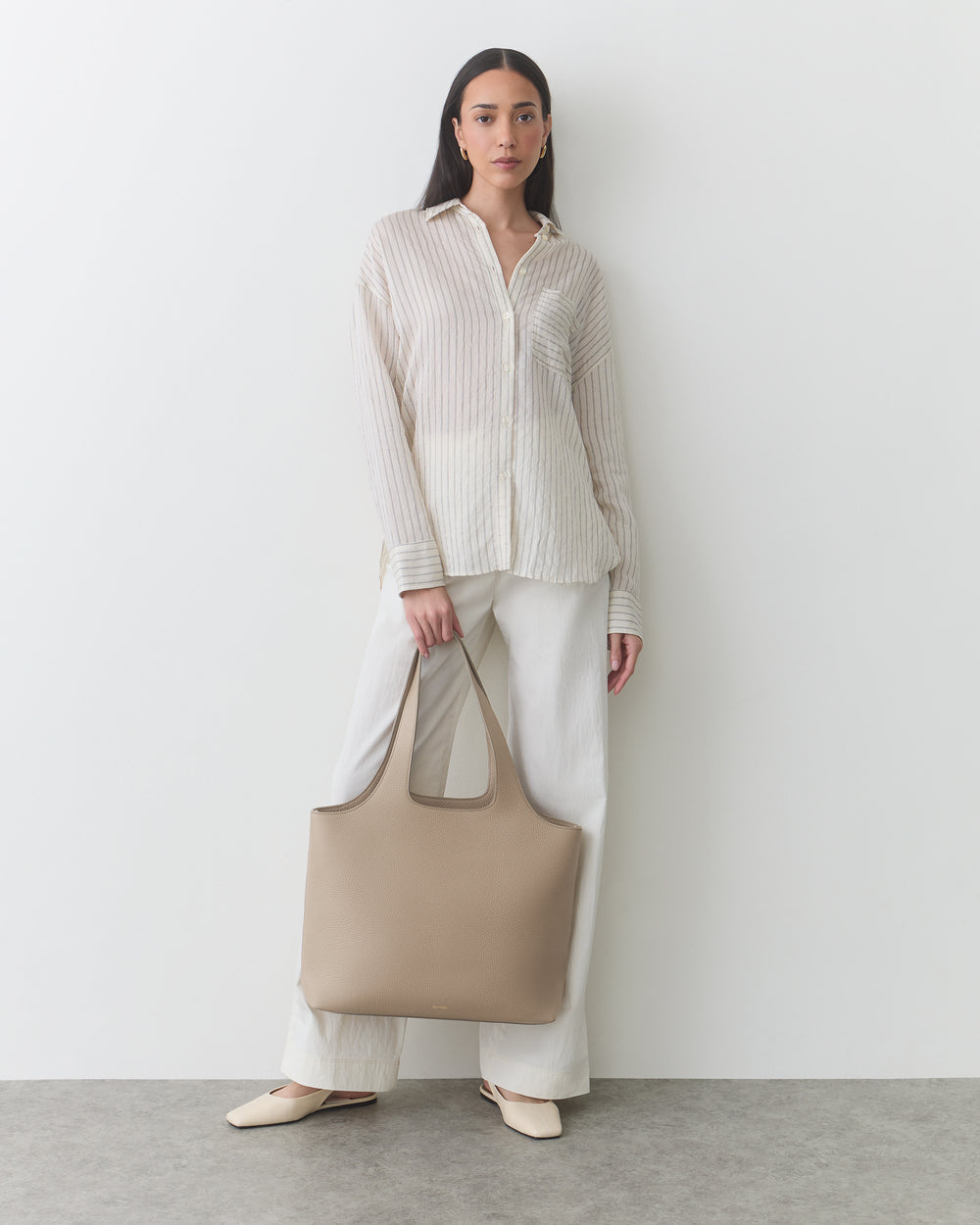 Person standing with a tote bag wearing a button-up shirt and pants.