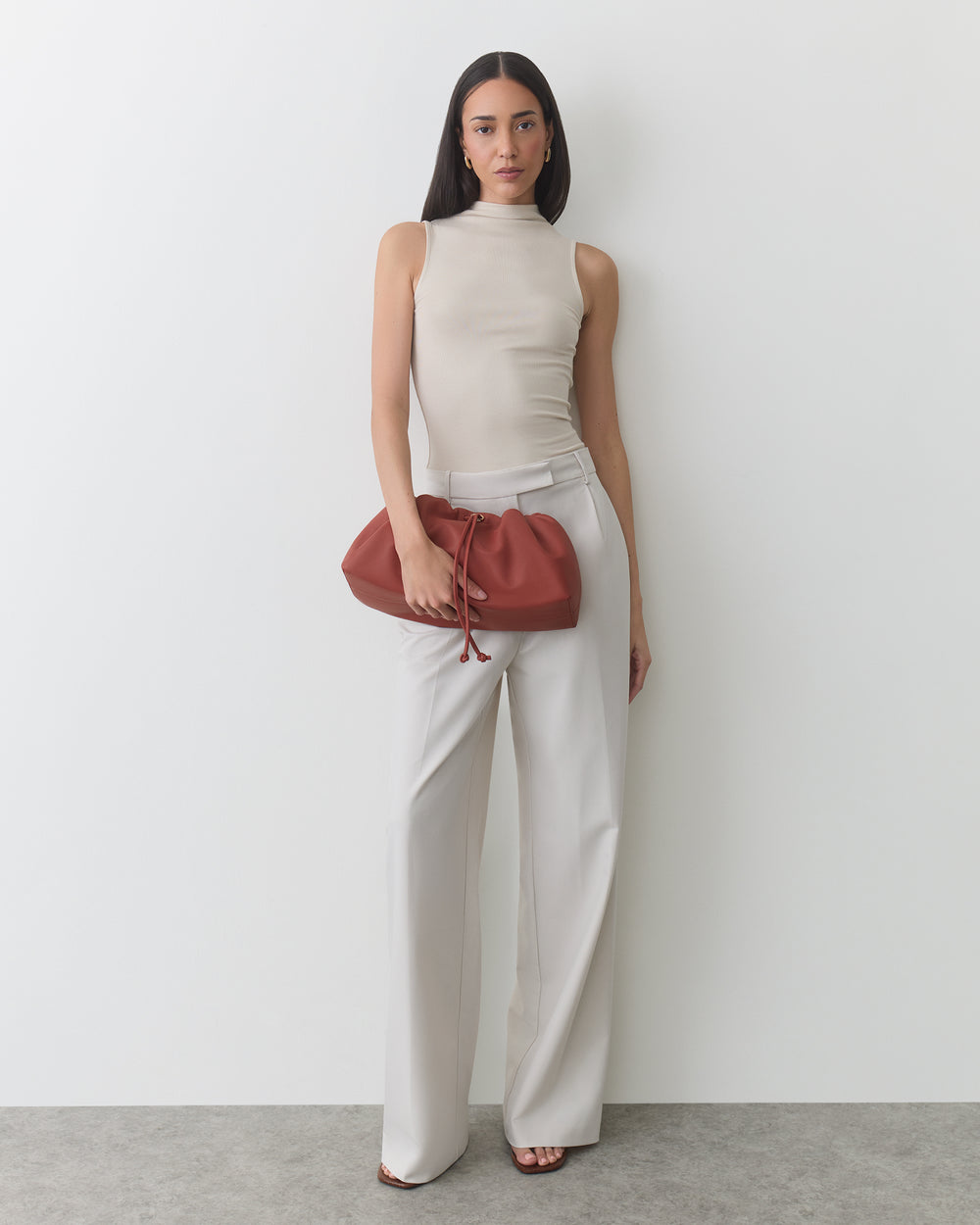 Person in sleeveless top and pants holding a gathered clutch bag.