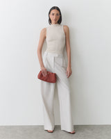 Person in a sleeveless top and wide-leg pants holds a clutch.