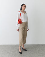 Person wearing a long-sleeve top, pants, holding a shoulder bag, standing indoors.
