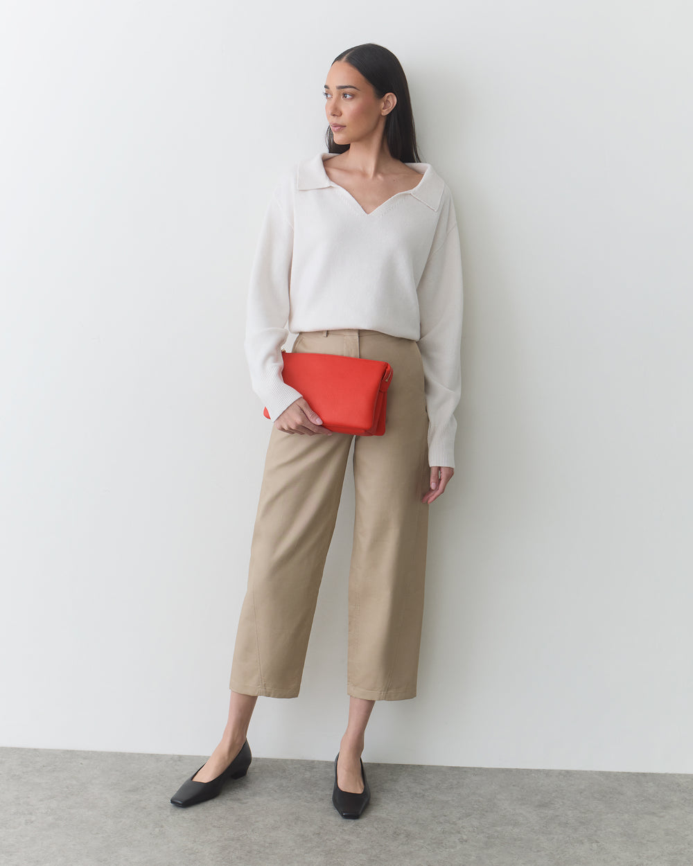 Person standing against a wall holding a clutch with one hand in pocket.