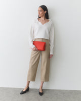 Person standing against a wall holding a clutch with one hand in pocket.