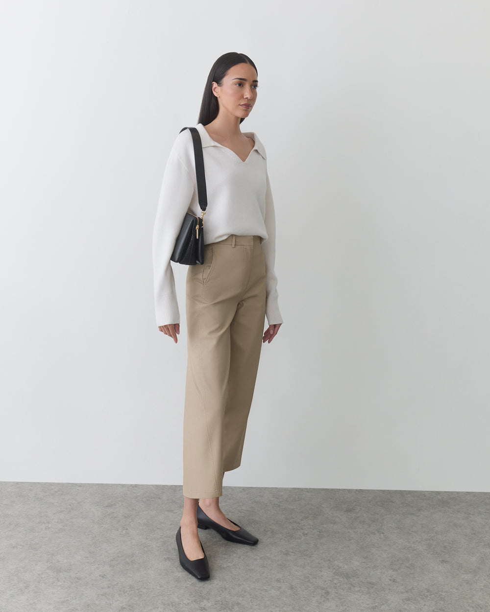 Person standing with a shoulder bag, wearing a long-sleeve top and pants.