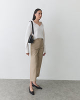 Person standing with a shoulder bag, wearing a long-sleeve top and pants.