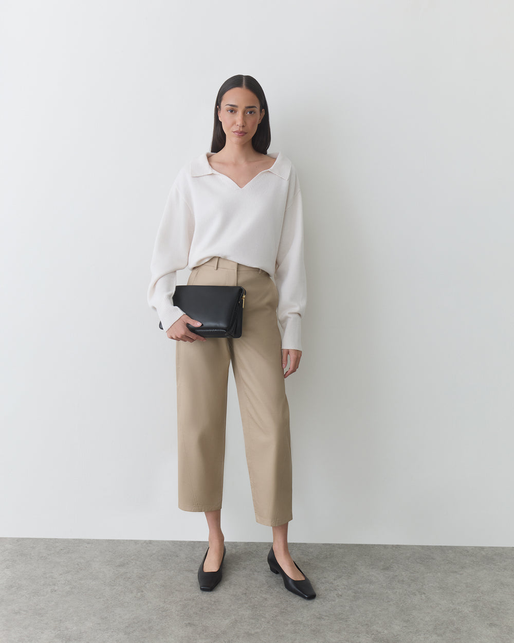 Person in blouse and pants holding a small bag, standing against a plain background.