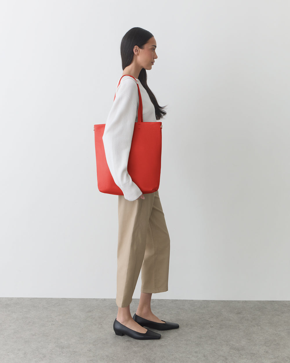 Person carrying a large tote bag and standing against a plain background.
