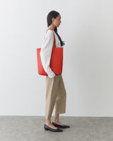 Person carrying a large tote bag and standing against a plain background.