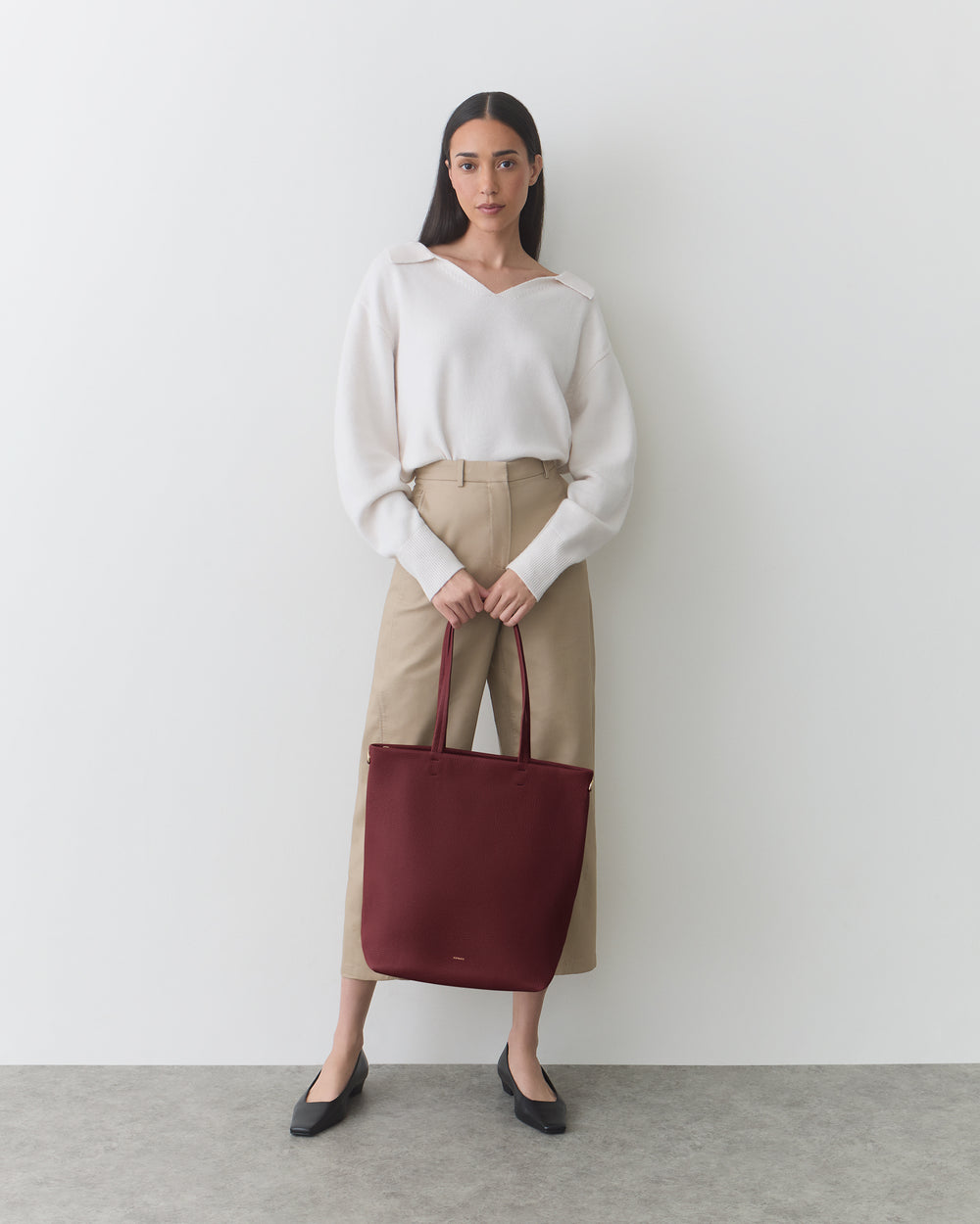 Person holding a large tote bag, standing against a plain background.