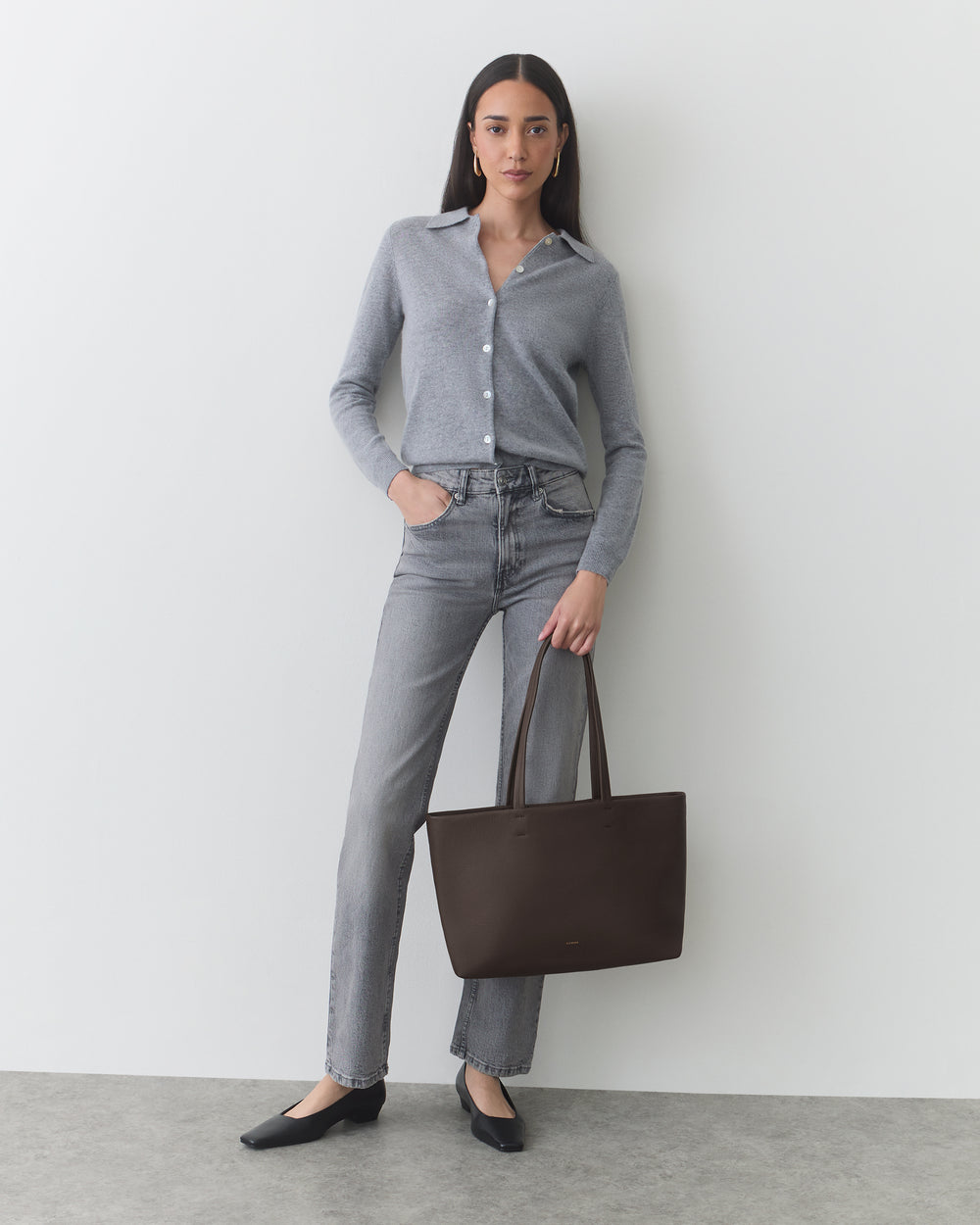 Person standing, wearing casual outfit, holding a tote bag, and looking at the camera.