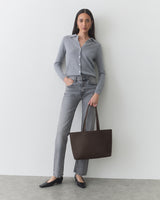 Person standing, wearing casual outfit, holding a tote bag, and looking at the camera.
