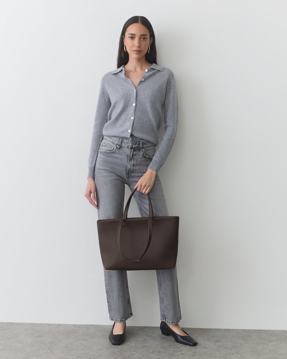 Person standing with a large handbag, wearing a shirt, jeans, and shoes.
