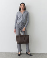 Person standing with a large handbag, wearing a shirt, jeans, and shoes.