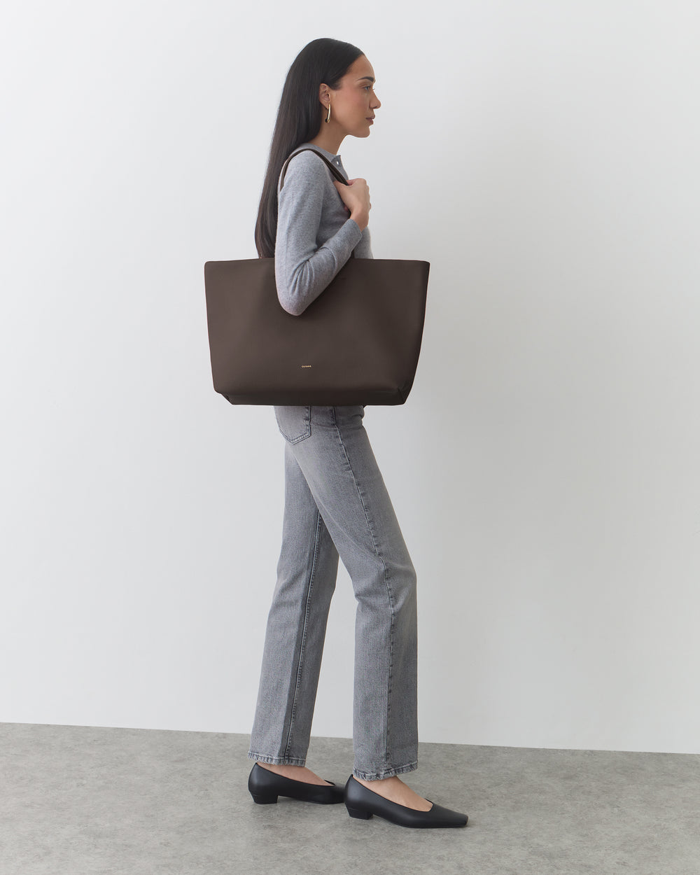 Person carrying a large tote bag, wearing a fitted top and jeans, standing sideways.
