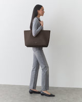 Person carrying a large tote bag, wearing a fitted top and jeans, standing sideways.