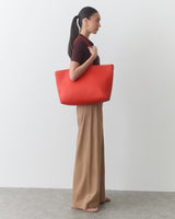 Person standing with large shoulder bag, wearing a short sleeve shirt and wide-leg pants.