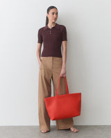Person wearing polo top and pants holds a large tote bag.