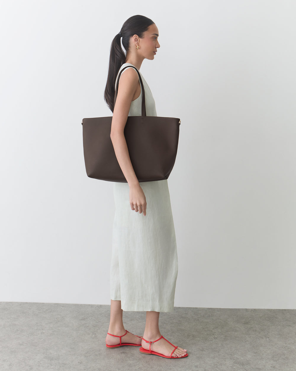 Person in sleeveless dress holding large bag, wearing strappy sandals.
