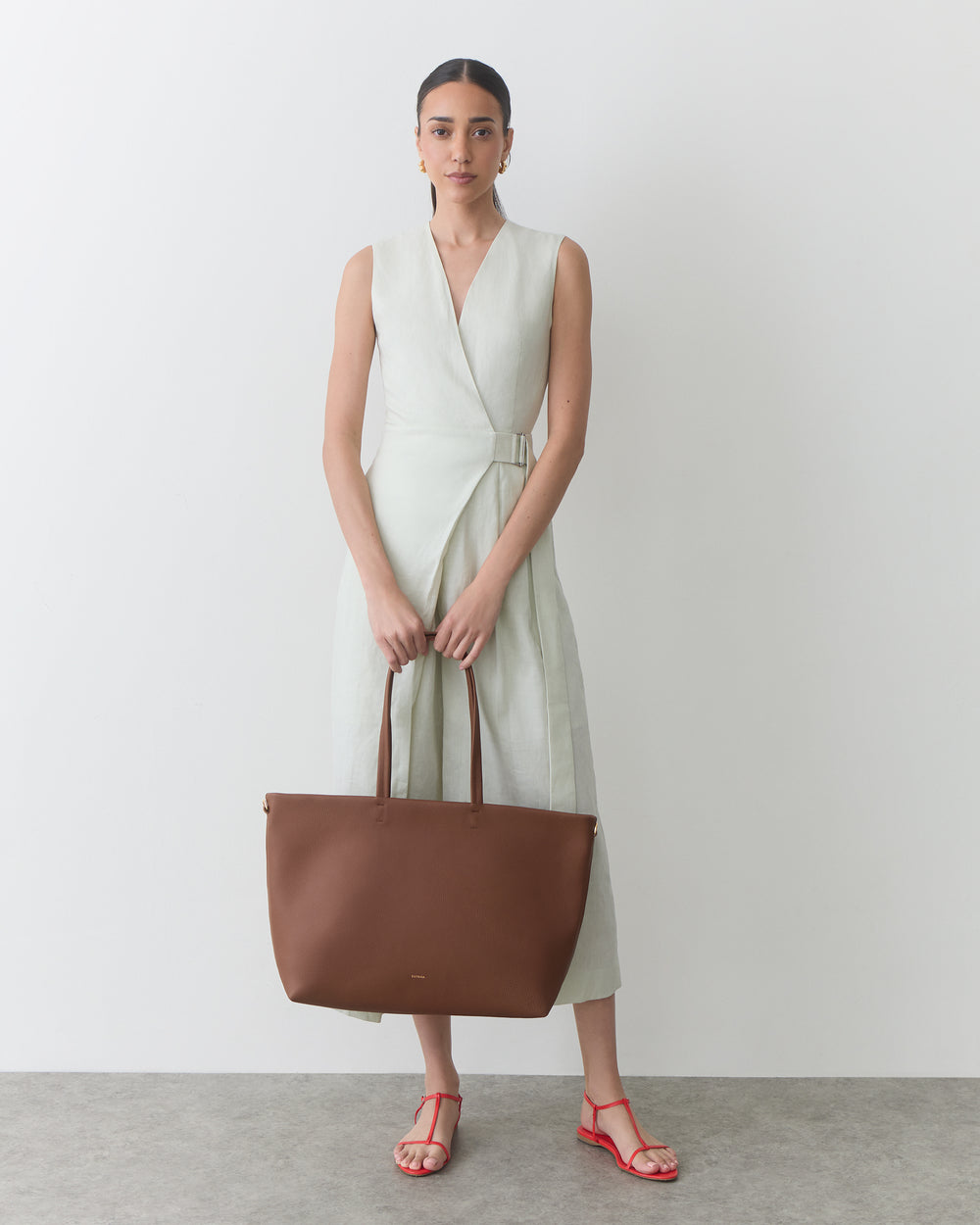 Person wearing a sleeveless dress holding a large tote bag.