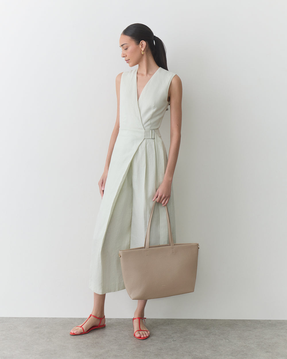 Person in a sleeveless dress holding a large handbag, wearing strappy sandals.