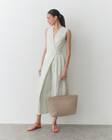 Person in a sleeveless dress holding a large handbag, wearing strappy sandals.